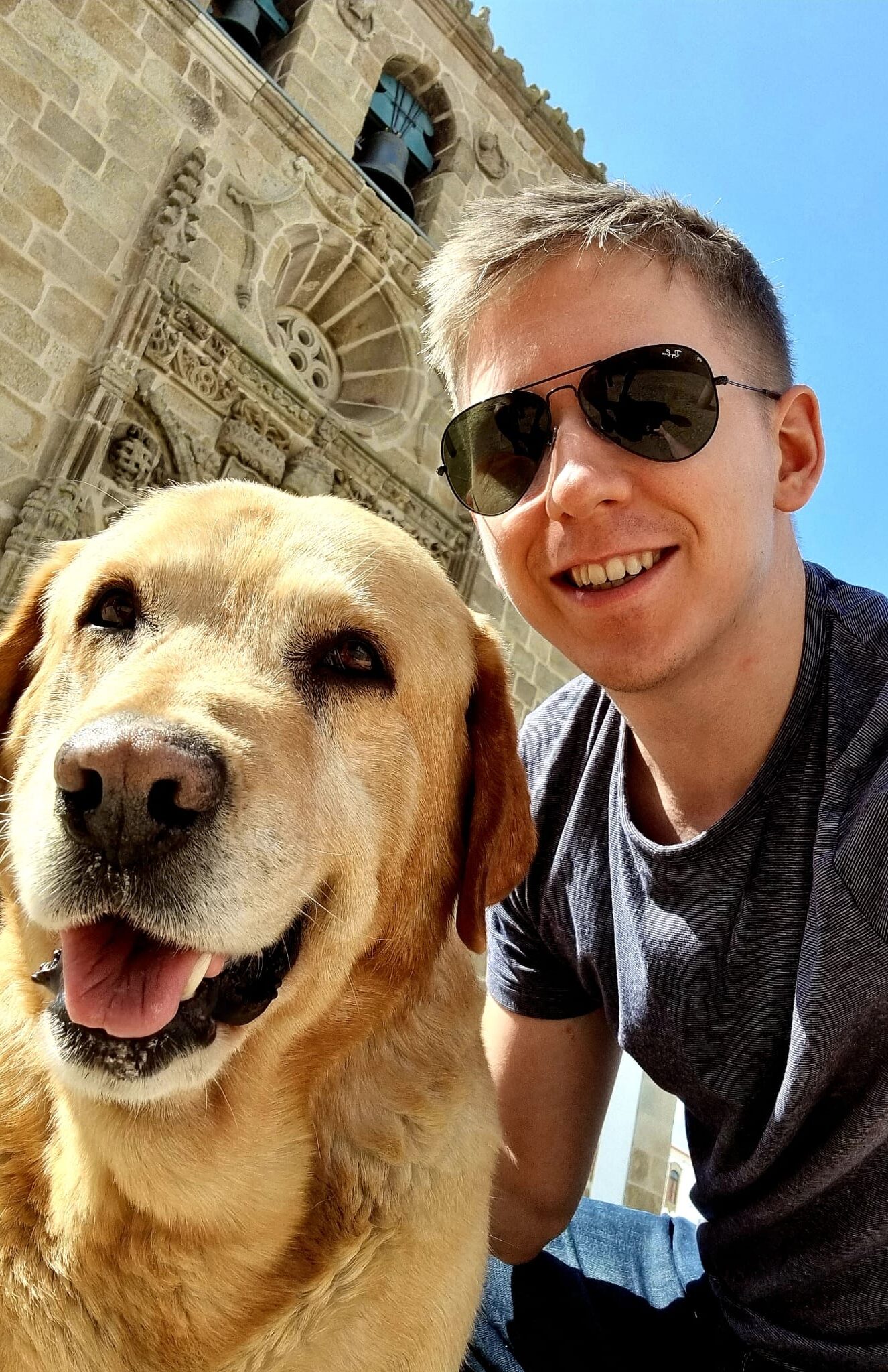 Tapio Kauranen in sunglasses, smiling beside a pale dog in front of an old stone church on a sunny day